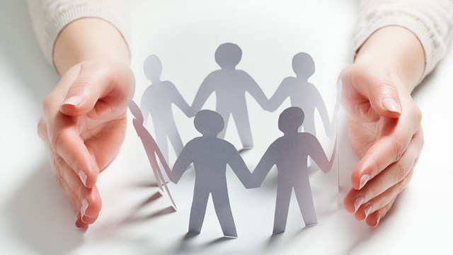 Paper people surrounded by hands in gesture of protection. Concept of insurance, social protection and support.