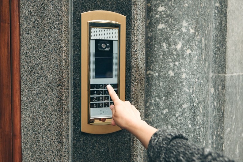 A female hand presses the buttons on the intercom for access inside.