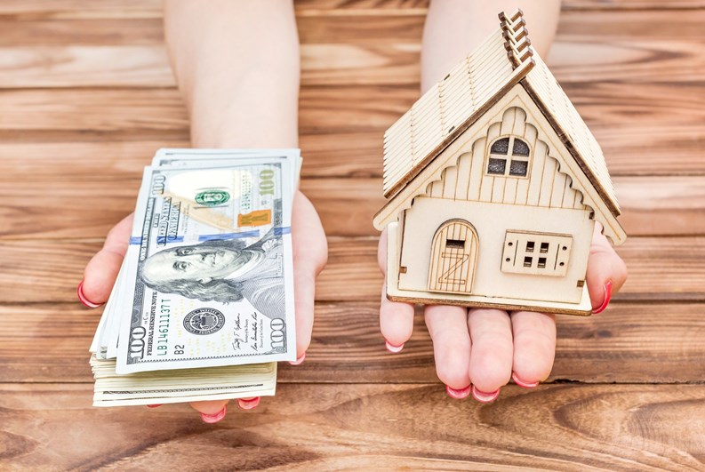 Woman's hands holding money and model of house over wooden table.