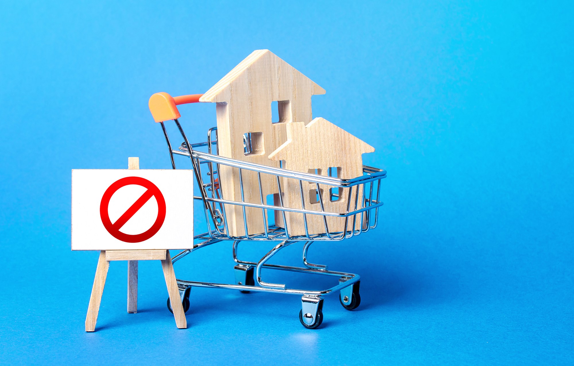 Houses in a shopping cart and easel red prohibition sign NO. Inaccessibility, lack housing, deficit. Seizure, freezing of assets by a bank, court. Expensive maintenance, impossibility of restoration