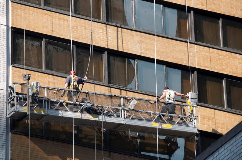 New York, New York, USA - August 5, 2010: Two men washing windows on a skyscraper. Working platform is raised and lowered by ropes.