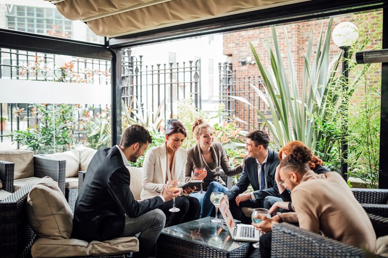 Group of business people are discussing their work in a bar courtyard after work. They are drinking cocktails and using technology.