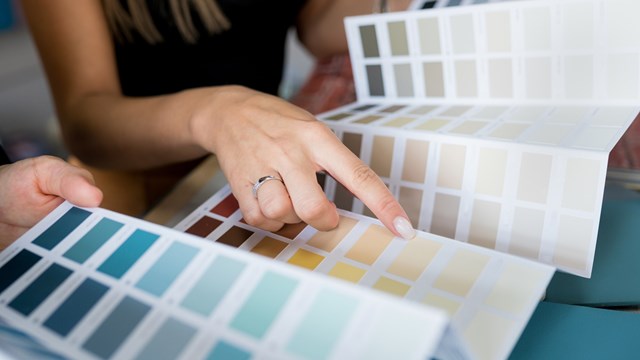Close-up of two women choosing samples of wall paint. Interior designer consulting a client looking at a color swatch. House renovation concept