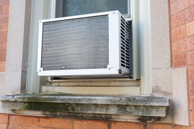 A simple window air conditioning unit seen from the outside on a brick urban residential building