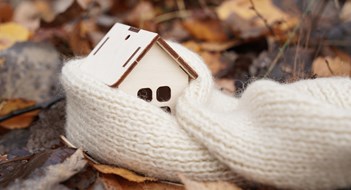 Winterization Medicine and weather concept. A wooden house wrapped in a scarf stands on fallen leaves.