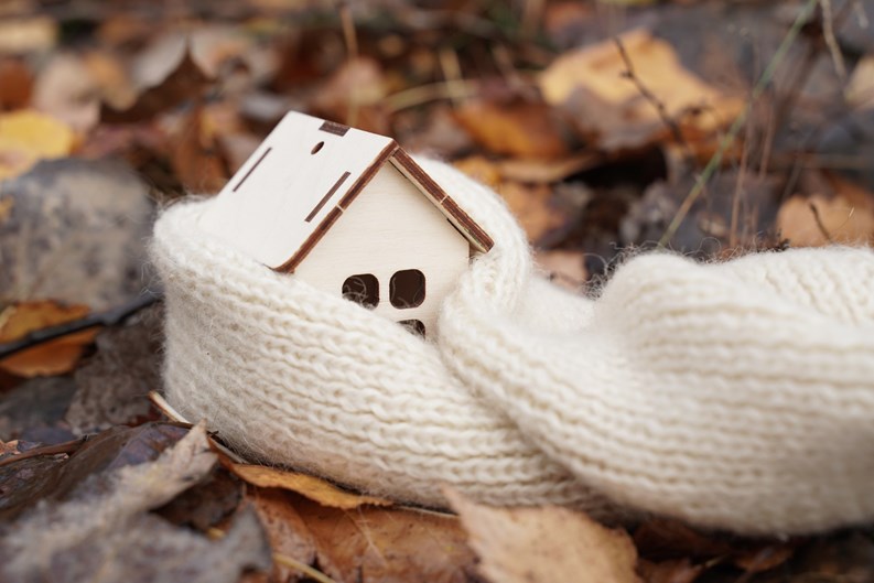 Medicine and weather concept. A wooden house wrapped in a scarf stands on fallen leaves.