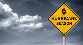 Hurricane Season is Here Yellow caution sign with black hurricane symbol, stormy sky in background