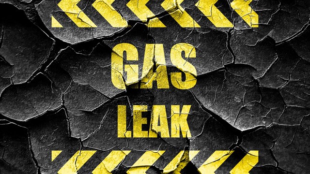 'GAS LEAK' warning sign in yellow block lettering on cracked black background