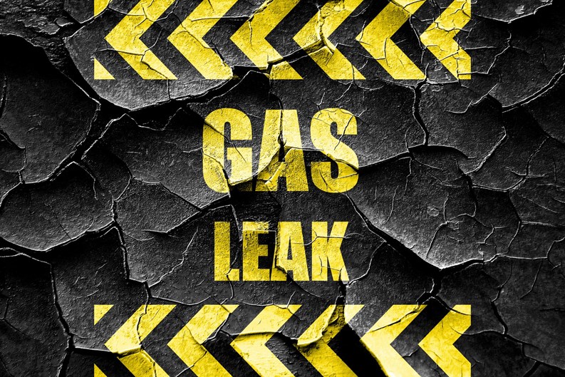 'GAS LEAK' warning sign in yellow block lettering on cracked black background 