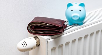 Fuel Prices Soar for  Co-ops, Condos, & HOAs A stuffed wallet lying on the radiator and a small blue piggy bank, The concept of rising apartment heating costs