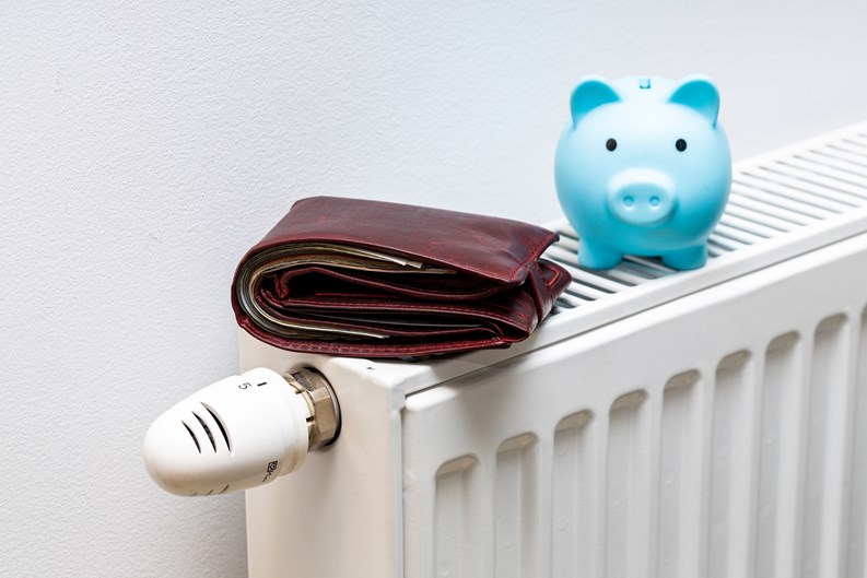 A stuffed wallet lying on the radiator and a small blue piggy bank, The concept of rising apartment heating costs