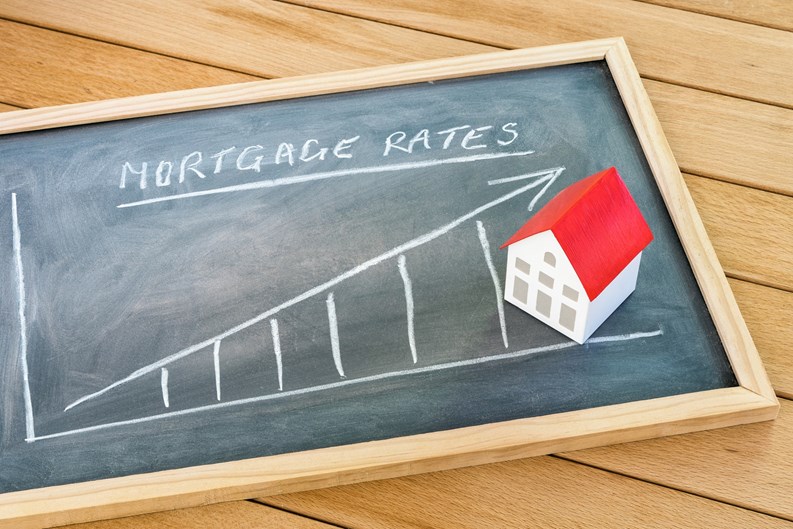 Graph representing the rise in mortgage interest rates drawn on a chalkboard lying on a wooden table. A model of a house with a red roof is on the chalkboard. Finance and real estate concept.