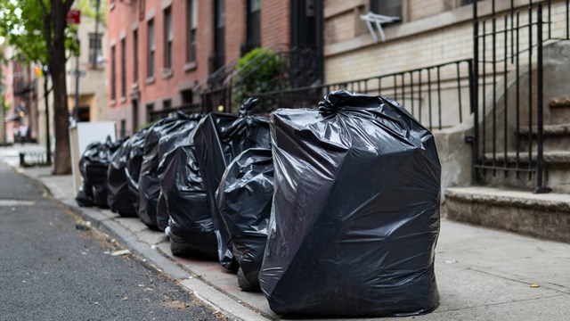 A row of black garbage bags along a residential street and sidewalk waiting to be picked up in Greenwich Village of New York City