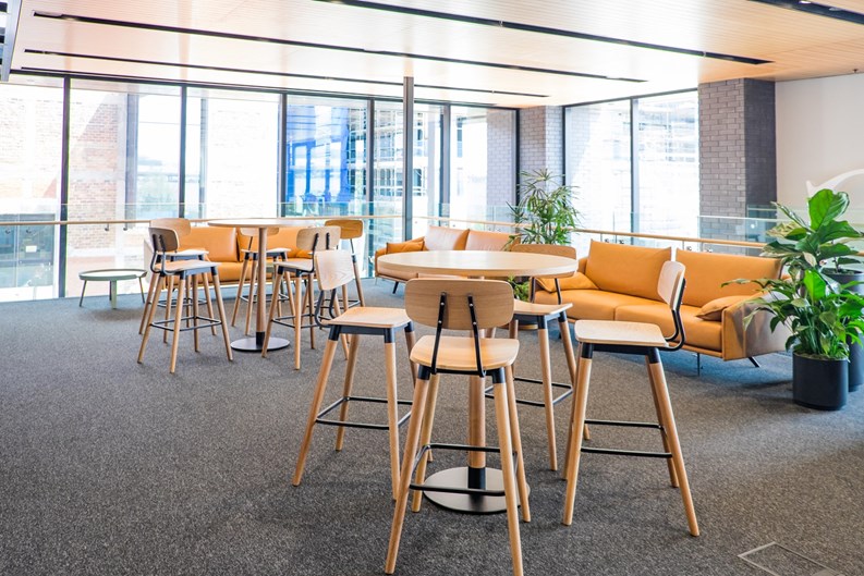 Meeting area in a modern creative coworking space with couch, sofa, bar stools, leaner tables, carpet. No people, modern building interior. 