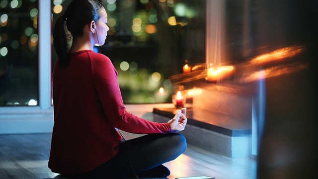 Girl doing yoga training at home at night. Young Latin American woman meditating using an app on smartphone.