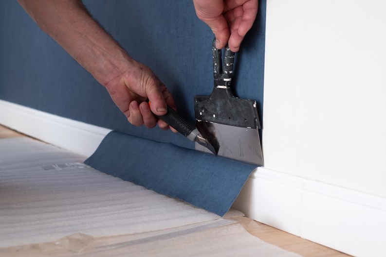 Man cutting wallpaper. Maintenance repair works renovation in the flat. Restoration indoors.