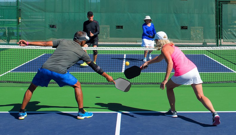 colorful action image of two couples playing pickleball in a mixed doubles match