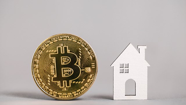 Kiev, Ukraine - May 18, 2021: Buying Property with Cryptocurrency. Buying real estate with bitcoin. Gold bitcoin coin, model house on gray background. property. Copy space.