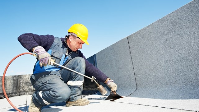 Roofer installing Roofing felt with heating and melting roll of bitumen roll by torch on flame