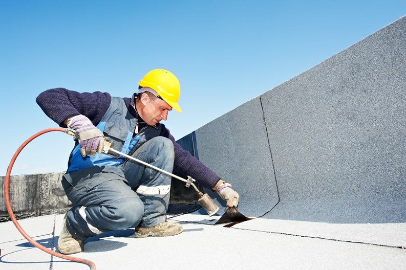 Roofer installing Roofing felt with heating and melting roll of bitumen roll by torch on flame