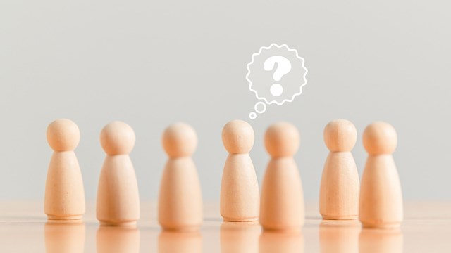 Wooden figurine as person who have questions and need help solving the problems among crowd people. Man has no idea on wood table. Business marketing and Creative solution concept.