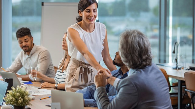 Two business people shaking hands while sitting in meeting room. Businesswoman shake hands to businessman. Portrait of happy smiling woman signing off deal with an handshake.