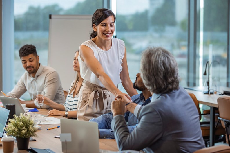 Two business people shaking hands while sitting in meeting room. Businesswoman shake hands to businessman. Portrait of happy smiling woman signing off deal with an handshake.