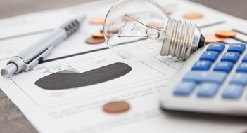 Improving Energy Efficiency A light bulb, a pen, a calculator and some copper euro cent coins lie on top of an electricity bill.
