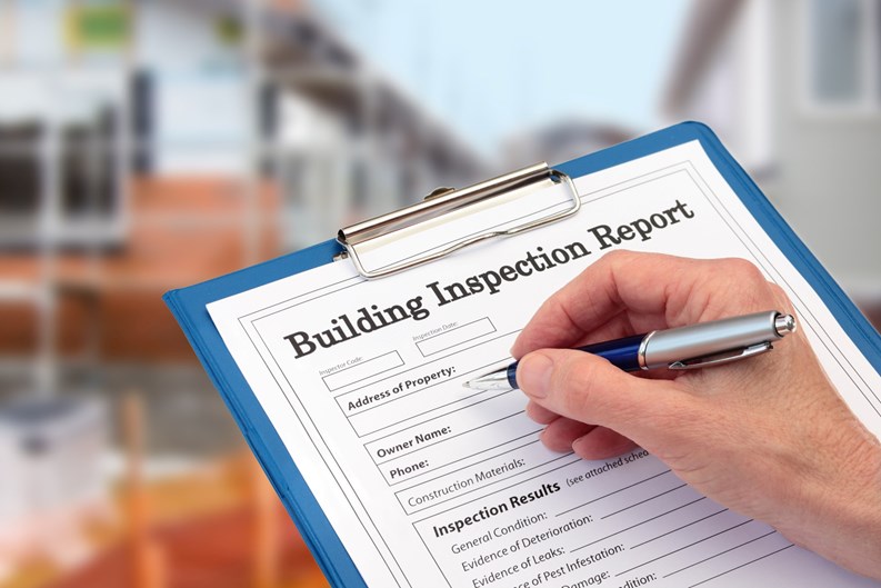 Buiding Inspector completing an inspection form on clipboard beside new build construction