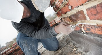 Complying with Parapet, Garage and Gas-Pipe Inspections Construction mason uses trowel to add mortar to brick joint.