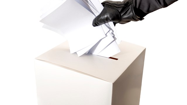 Electoral fraud and hacked elections concept with a hand wearing a leather glove and stuffing a ballot box isolated on white background with copy space and a clipping path cut out