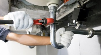 Water Infiltration & Leak Management Technician plumber using a wrench to repair a water pipe under the sink. Concept of maintenance, fix water plumbing leaks, replace the kitchen sink drain, cleaning clogged pipes is dirty or rusty.