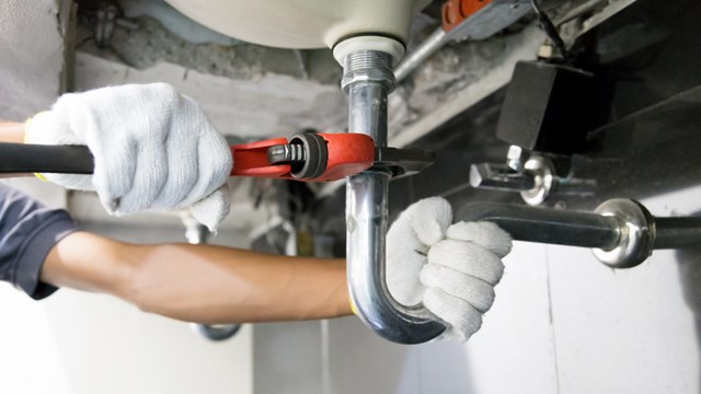 Technician plumber using a wrench to repair a water pipe under the sink. Concept of maintenance, fix water plumbing leaks, replace the kitchen sink drain, cleaning clogged pipes is dirty or rusty.