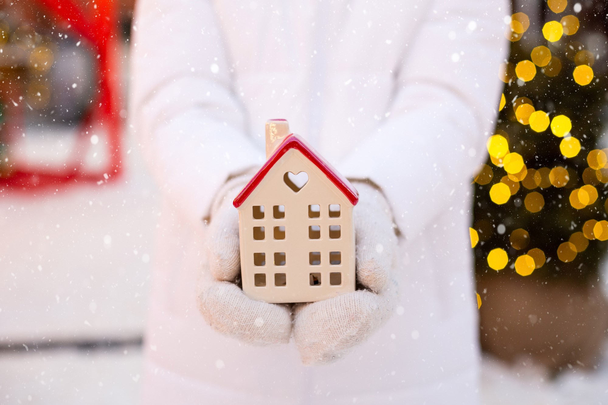 House, miniature cottage in hands of woman wearing mittens and warm clothes outdoor in snow. Deal for real estate, purchase, construction, relocation, mortgage. Cozy home, Christmas, new year booking