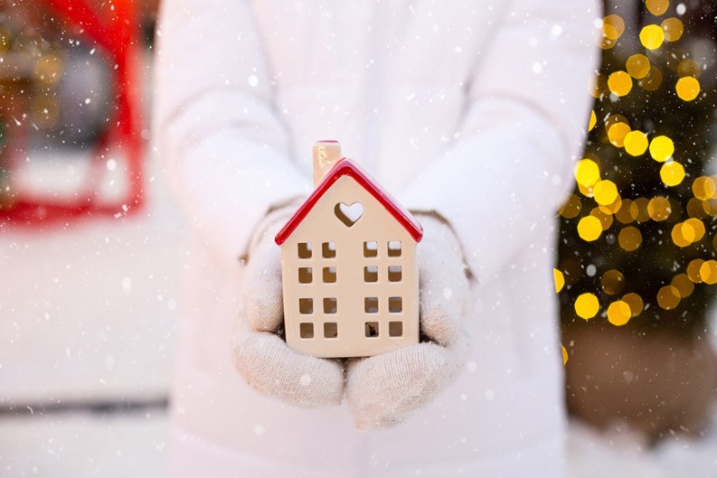 House, miniature cottage in hands of woman wearing mittens and warm clothes outdoor in snow. Deal for real estate, purchase, construction, relocation, mortgage. Cozy home, Christmas, new year booking